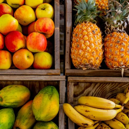 Colorful display of apples, pineapples, bananas, and papayas in wooden crates at a market.